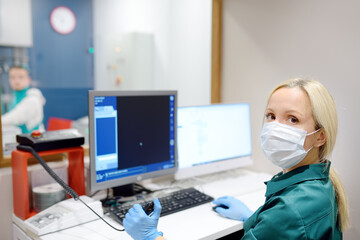 Female radiologist is going to take X ray of patient in X-ray room of modern clinic. Close up photo of doctor hand presses button for execute of medical examination