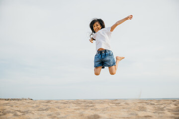 Portrait of a small girl jumping on the beach filled with joy and excitement. Playful motion...