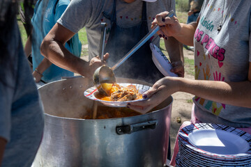 Manos sirviendo guiso de pollo en un comedor popular al aire libre, primer plano, plato y cucharón