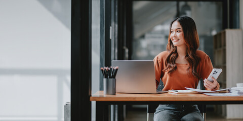 A woman is sitting at a desk with a laptop and a cell phone. She is smiling and she is happy