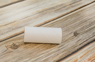 An empty toilet tissue cardboard tube lying horizontally on a wooden tabletop