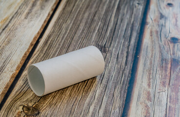 An empty toilet tissue cardboard tube lying on a wooden tabletop