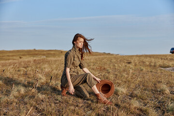 Woman sitting in the middle of a field with a brown hat on her head, enjoying nature's beauty