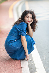 Outdoors a curly-haired Chinese beauty in a denim skirt