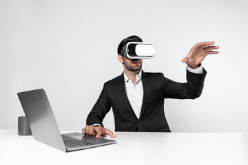 Skilled business man looking at data analysis while sitting at table with laptop and wearing VR glasses. Project manager working by using virtual reality system or connecting at metaverse. Deviation.