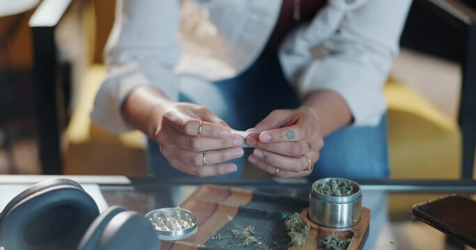 Rolling paper, marijuana and prepare with hands in home for smoking with relax or high with person. Joint, cannabis and pot with hemp on weekend for 420 with natural cbd or weed addiction at table