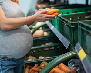 Pregnant woman buys carrots in the store. 