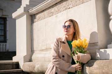 Woman holding yellow tulips, leaning against stone wall. Women's holiday concept, giving flowers.