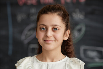 Closeup portrait of modern Middle Eastern girl with gray eyes standing against blackboard in...