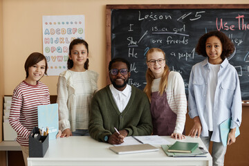 Group of multi-ethnic kids and their African American teacher of English language posing for camera...