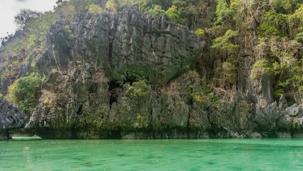 Picturesque karst rocks surround the emerald bay. There is tropical vegetation on the steep slopes....