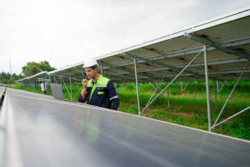 A man in a green and white uniform is standing in front of a solar panel. He is holding a cell...
