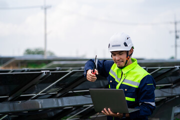 A man in a yellow and blue uniform is looking at a laptop computer. He is wearing a hard hat and...