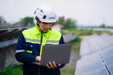 A man wearing a yellow and green jacket is looking at a laptop. He is wearing a hard hat and safety...