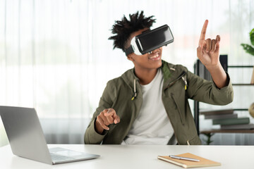 Young African American looking through VR pointing zoom for data online meeting hologram metaverse world connecting digital futuristic technology virtual reality at meta modern office. Contrivance.
