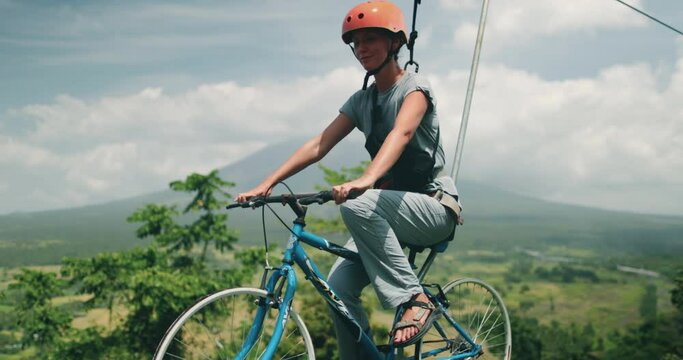 A womani riding a bike on top of a zip line over the beautiful volcanic crater lakes in the Philippines. The daring act combines biking and zip-lining for an adventurous experience.