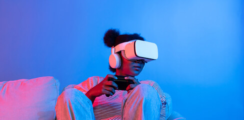 Smiling African American playing gaming player wearing VR controlling joystick on 3D hologram screen isolated vibrant neon light connecting digital futuristic technology metaverse world. Contrivance.