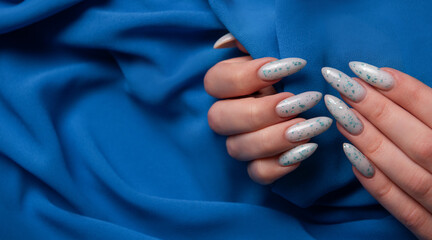Female hands with blue nail design on blue textile background.