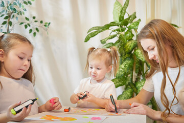 Young mother or babysitter, little daughter, sister teenager girl drawing at table in room. Painting, doing homework, family enjoying leisure at home