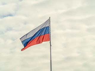 Russian tricolor flag waving in the wind against a blue sky.