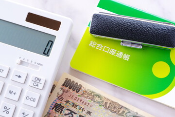 テーブルの上に置かれた銀行の預金通帳と印鑑、1万円札、電卓
