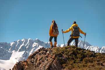 Two active hikers or tourists with backpacks are standing on view point with a great view at white...
