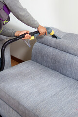 vertical shot of A man is cleaning a couch with a steam cleaner.