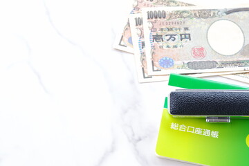 テーブルの上に置かれた銀行の預金通帳と印鑑、1万円札
