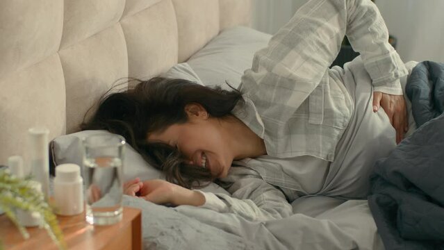 Woman lying on bed touch stomach pain menstrual period girl female pills medicine unhealthy poisoning ill hurting unwell abdomen bedroom body sickness ache discomfort belly hurt home painkiller drugs