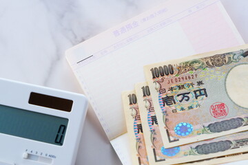 テーブルの上に開いた状態で置かれた銀行の預金通帳と、1万円札、電卓
