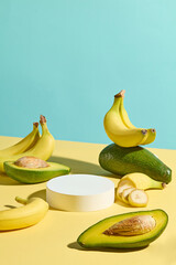 Creative design with high angle view at a yellow table containing fresh fruit like banana and avocado with a circular pedestal of white in center. Displaying or presentation space
