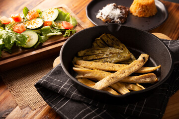 Roasted chicken breast cut into strips, roasted in a cast iron skillet accompanied by roasted nopales and fresh salad, served on a rustic wooden table. Simple and nutritious homemade recipe.