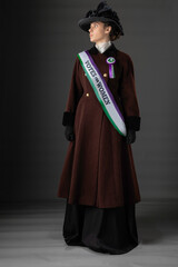 United Kingdom Victorian or Edwardian Suffragette wearing historically accurate purple and green sash and rosette against a plain studio backdrop