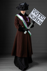 United Kingdom Victorian or Edwardian Suffragette wearing historically accurate purple and green sash and rosette against a plain studio backdrop