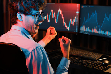 Successful business trader raising fist up with highest profit looking on global market online in...