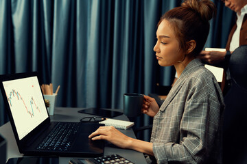 Businesswoman working on laptop with stock market to invest while drinking coffee at modern office...