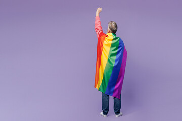 Fototapeta premium Full body back view elderly gay man 50s years old wears casual clothes wrapped in striped rainbow flag raise up hand clench fist isolated on plain purple background. Lifestyle LGBT June pride concept.