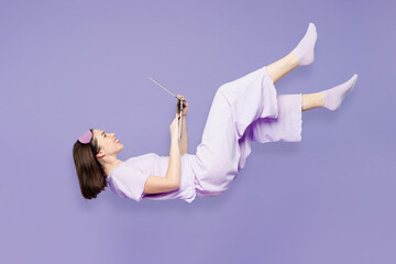 Full body young IT woman in pyjamas jam sleep eye mask rest relax at home fly fall hover over air...