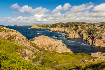 Rocky coast of Norway, mountains covered with moss and grass strong currents and dangerous cliffs. Cumulus clouds against a bright blue sky. Near Lindesnes Lighthouse, North Sea.