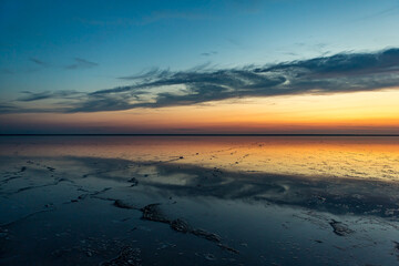 Sunset or sunrise on salt lake Elton (Russia) with mirror or reflection of high Altocumulus or Cirrocumulus clouds in the brine at golden hour. Evening or morning. Volrograd district.