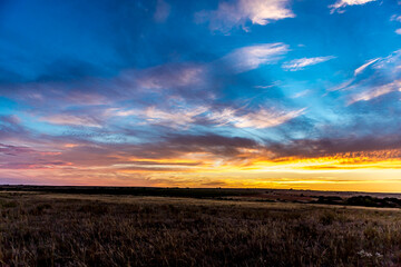 Sunrise or sunset in the Russian steppe at golden hour. Cumulostratus Cirrocumulus, Altocumulus and Stratus clouds. The sun is shining from behind a cloud. Red orange and white shades.