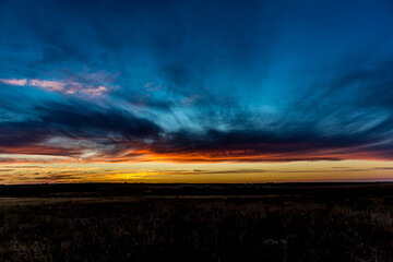 Sunrise or sunset in the Russian steppe at golden hour. Stratus, Cirrocumulus and Altocumulus clouds. The sun is shining from behind a cloud. Red orange and white shades. Morning or evening.