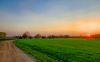 A peaceful and beautiful rural landscape at sunset with green fields and a dirt road, creating a serene scene