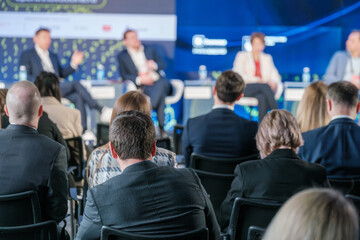 Rear view of audience attentively listening to a panel of speakers at a professional business...