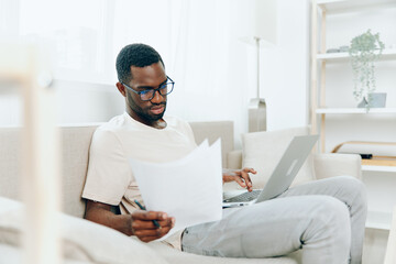 A Young African American Man Working on his Laptop from the Comfort of his Modern Living Room