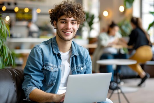 A young man is sitting on a couch with a laptop in front of him