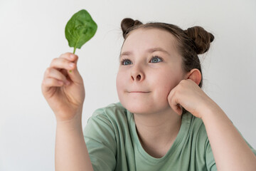 Pretty little girl holding a spinach leaf, looking at it. Concept of healthy food and natural...