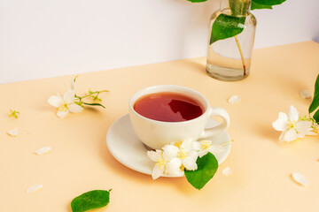 A cup of tea and jasmine flowers on beige table. Closeup
