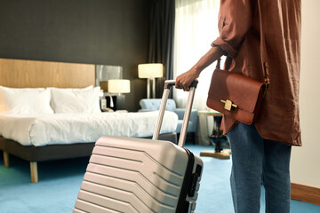 Cropped back view of African American woman entering hotel room and holding suitcase copy space