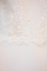 A closeup view of a delicate white lace fabric featuring intricate floral embroidery and shimmering...
